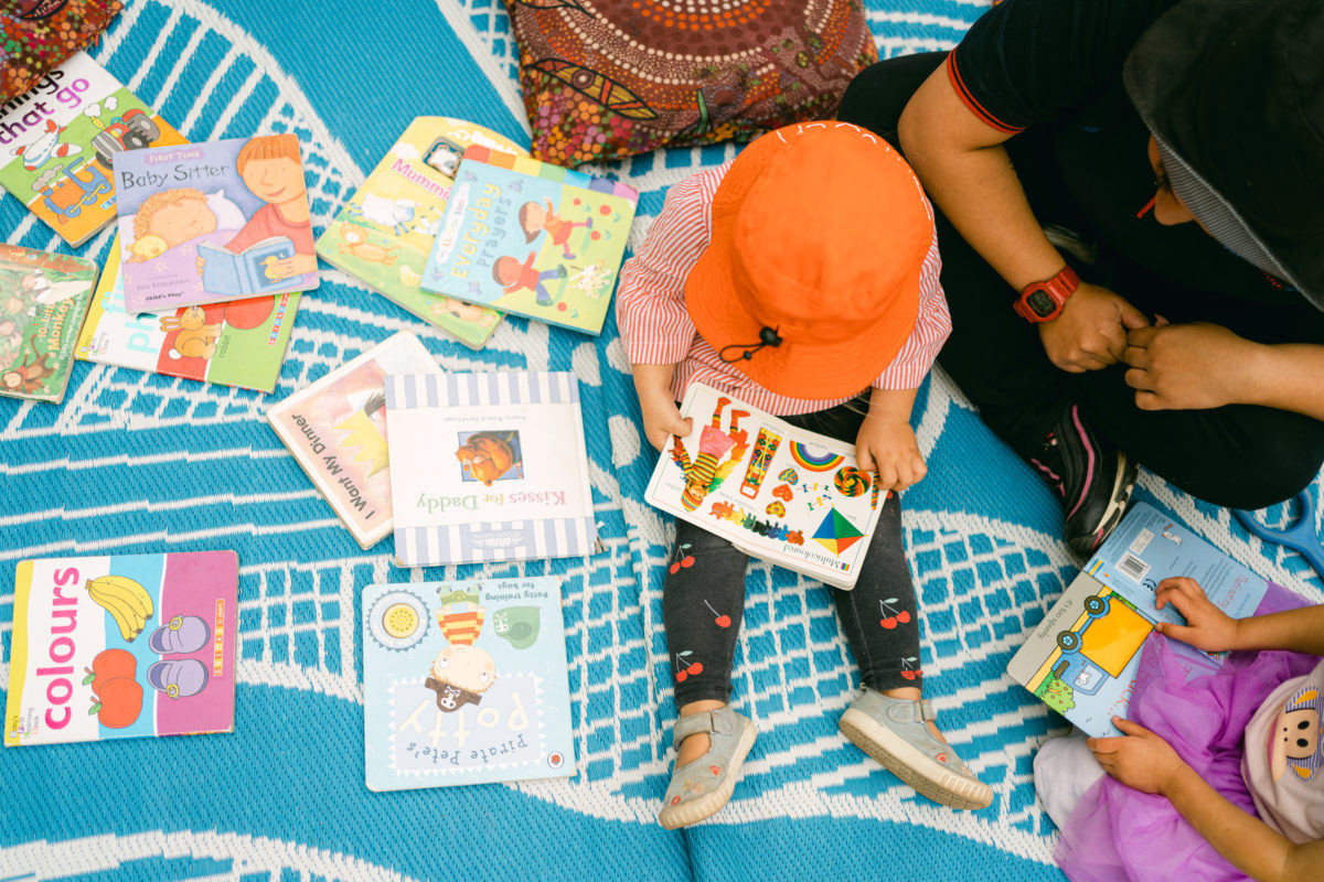 Carer and children reading books on a rug