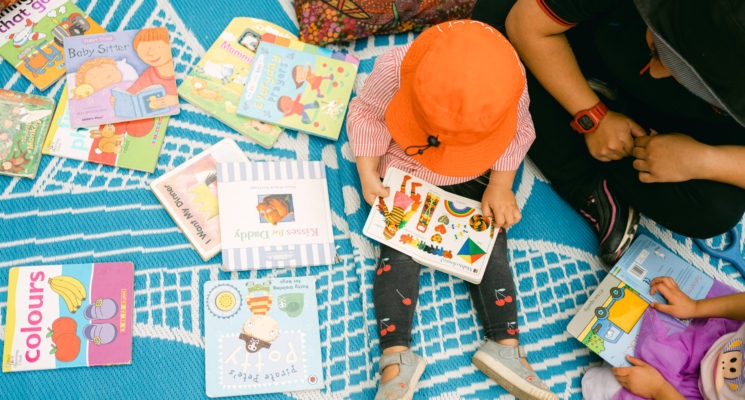 Carer and children reading books on a rug