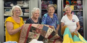 4 happy older woman holding up hand-made blankets