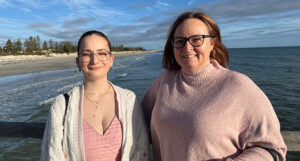 2 women in pink tops smiling standing in front of ocean
