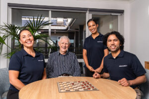 Carers sitting with an elderly man smiling, with a chessboard on the table