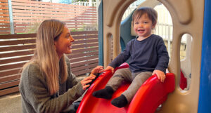 blonde woman smiling at young boy on slide