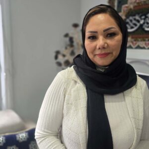 Woman in hijab white white top and black scarf on standing in her home