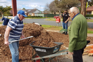 Two men use a wheelbarrow to transport landscaping materials