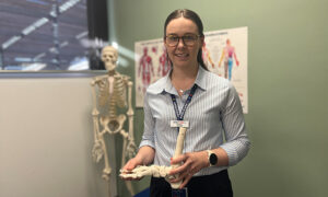 Young female podiatrist standing in clinic holding model foot