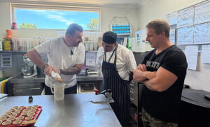 3 men standing in a kitchen pouring sauce into a container