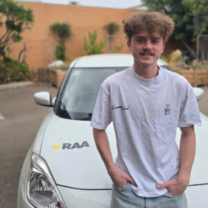 Young adult standing in front of RAA branded car with hands in his pocket