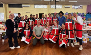 group photo of people in christmas outfits standing and smiling in a warehouse