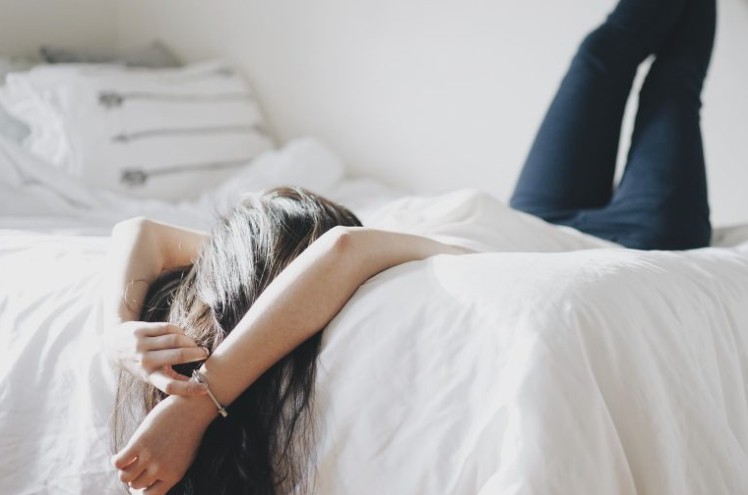 A person lying on their bed with their legs up against the wall and hands hanging off the bed
