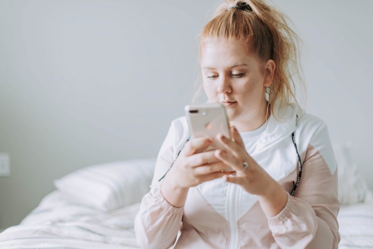 A lady using her phone while sitting on the bed