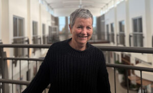 smiling woman in black sweater stands on balcony