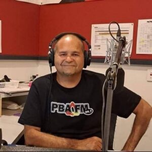 Man in black shirt sitting next to microphone and black headphones on