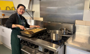Smiling woman in kitchen standing over oven tray on stove