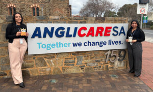 2 female workers standing either side of a sign that reads "AnglicareSA Together we change lives."