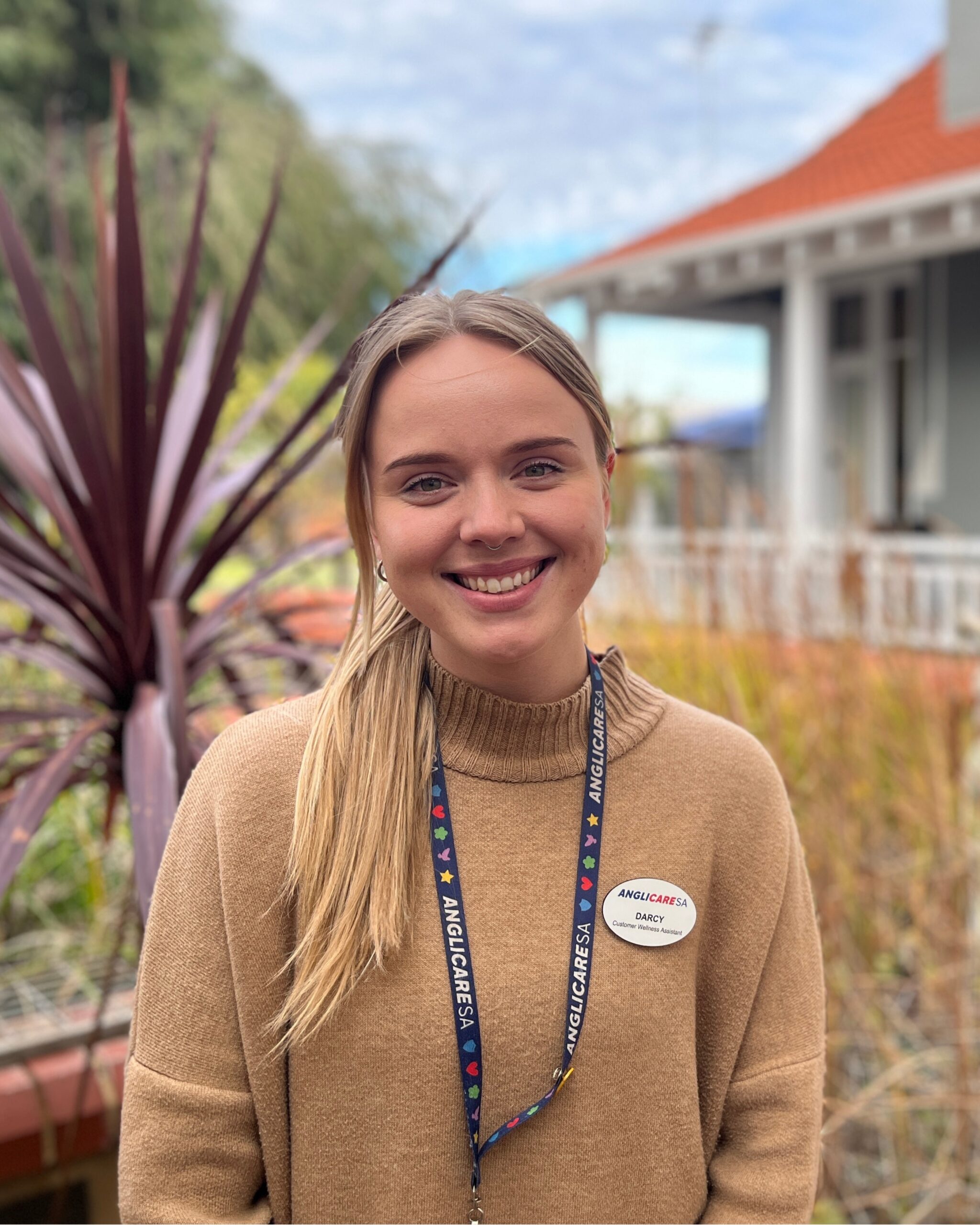 AnglicareSA employee, Darcy Kemp, is standing and smiling in the garden in front of a house.