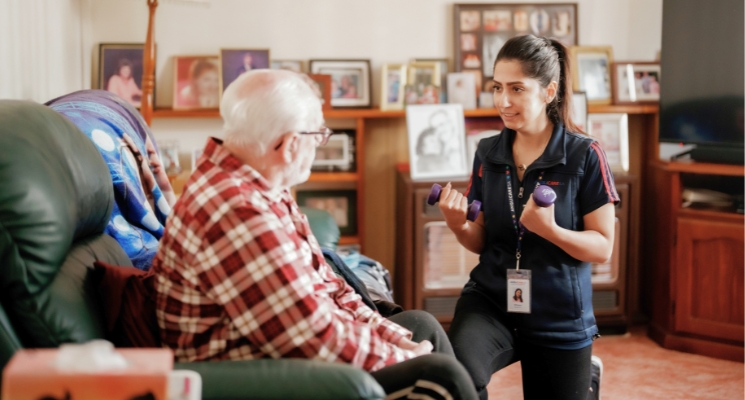 An aged care worker holds weights showing an older person how to exercise using them