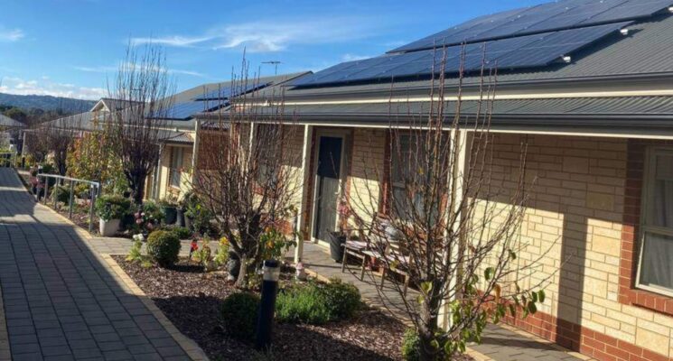 Community houses in a row with solar panels on the roof. The sky is clear blue and sunny.