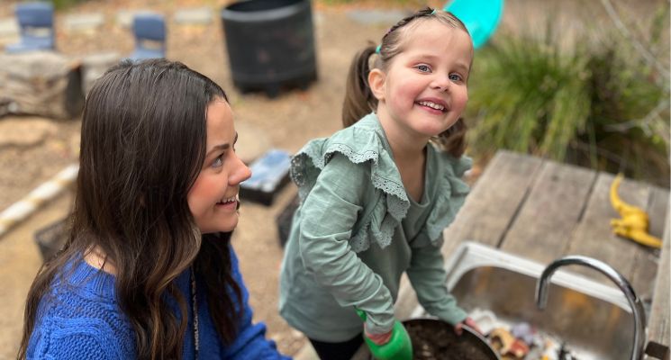 A young child plays outside with sandpit toys with her Speech Pathologist carer.