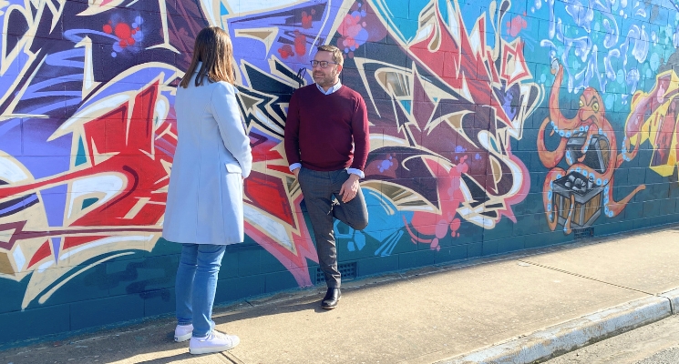 Two people having a conversation in front of a wall painted with street art.