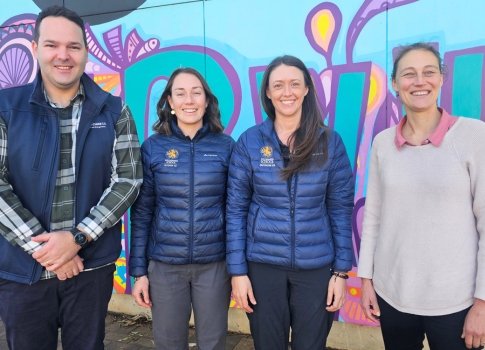 Luke, Rosie, Lauren and Rebecca are smiling and standing in front of a wall painted with a colourful street art mural.