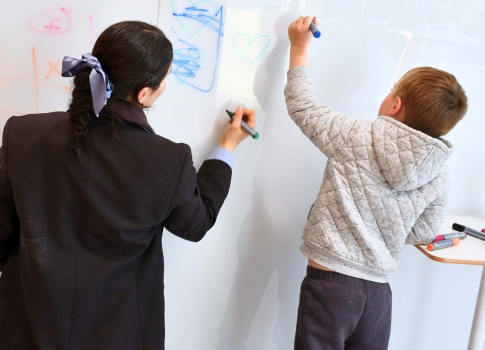 A student and a younger child write on a whiteboard.