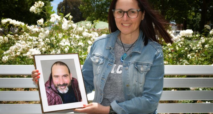 Jo sits on a white bench holding a photo of her husband Davide.