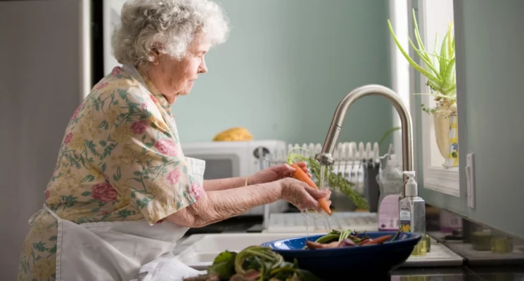 Older woman washing vegetables at kitchen sink.