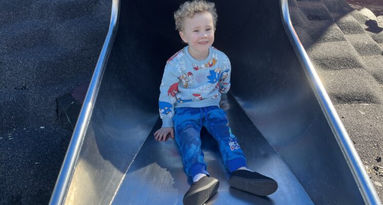 Rueben sitting on the slide smiling.