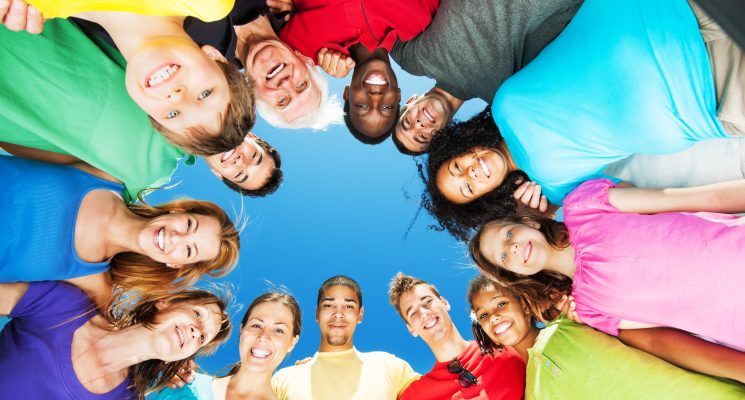 Group of embraced people standing in circle against blue sky.