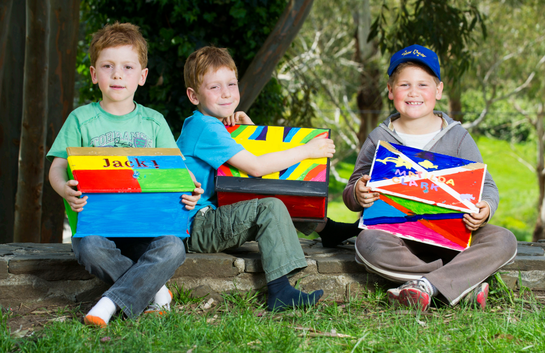 Three boys sit holding colourful boxes.