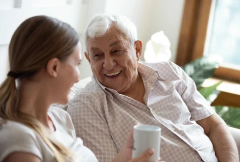 An older man and a younger women have a conversation over cups of coffee.